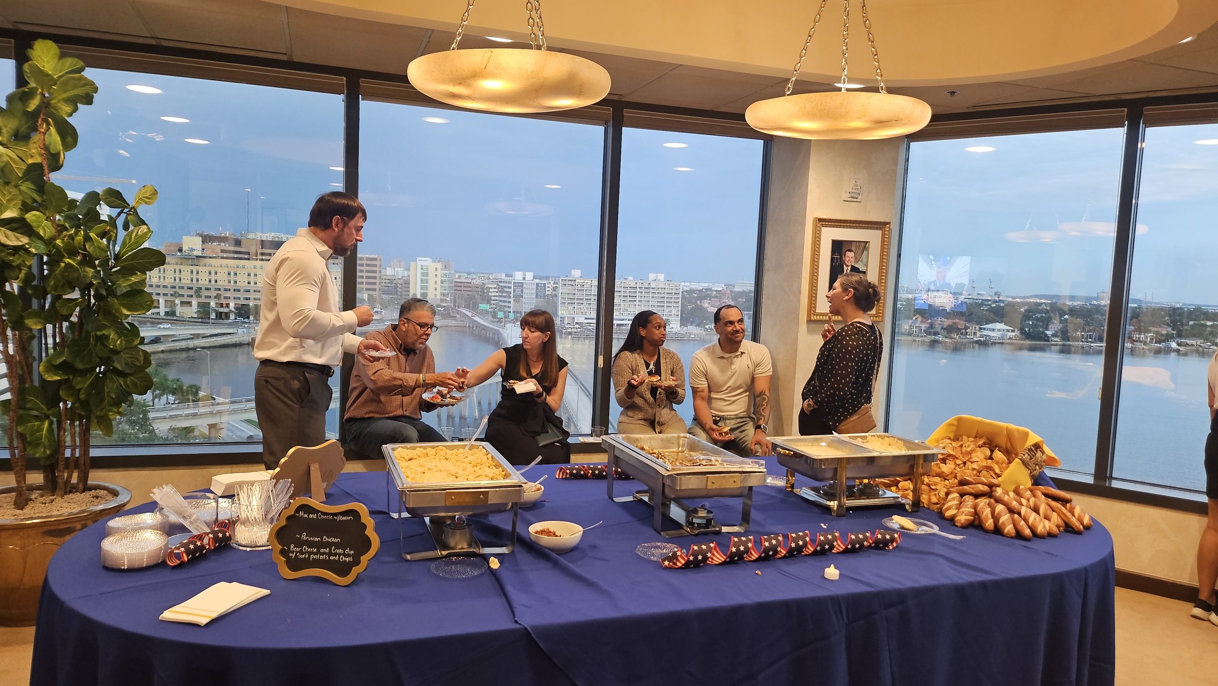 A staffed buffet with chafing dishes set up beside floor-to-ceiling windows overlooking the Tampa waterfront, guests helping themselves
