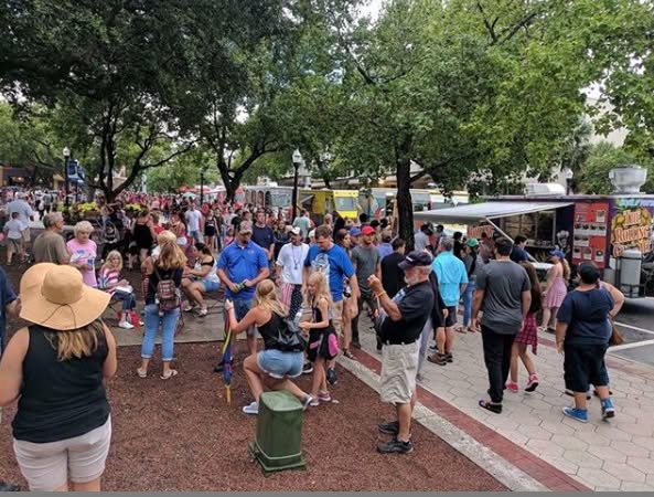 Large crowd of guests walking between food trucks at a shaded park event