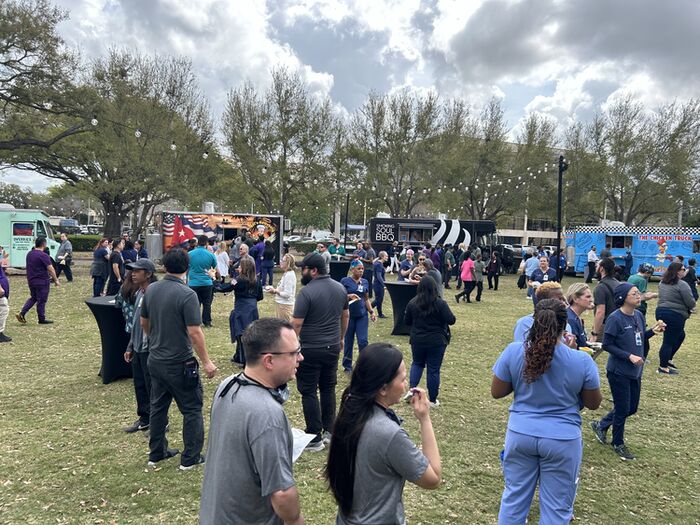 Corporate guests gathered on a lawn with a row of catering food trucks