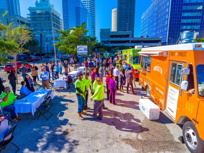 Food trucks and event staff serving a crowd on a downtown street lined with high-rise buildings